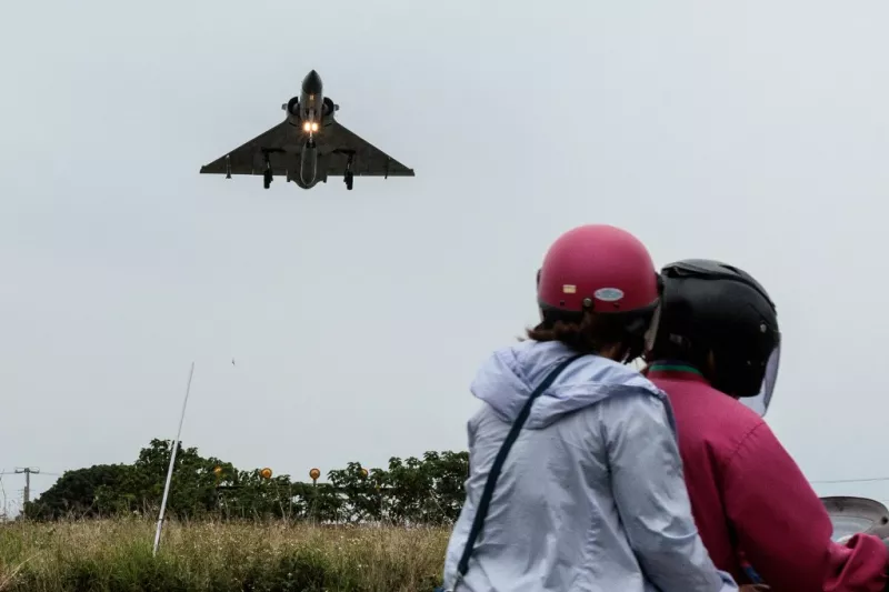 Dos personas viajan en una motocicleta mientras un avión de combate Mirage 2000 de la Fuerza Aérea de Taiwán se acerca para aterrizar en una base de la fuerza aérea en Hsinchu, en el norte de Taiwán, el 23 de mayo de 2024.