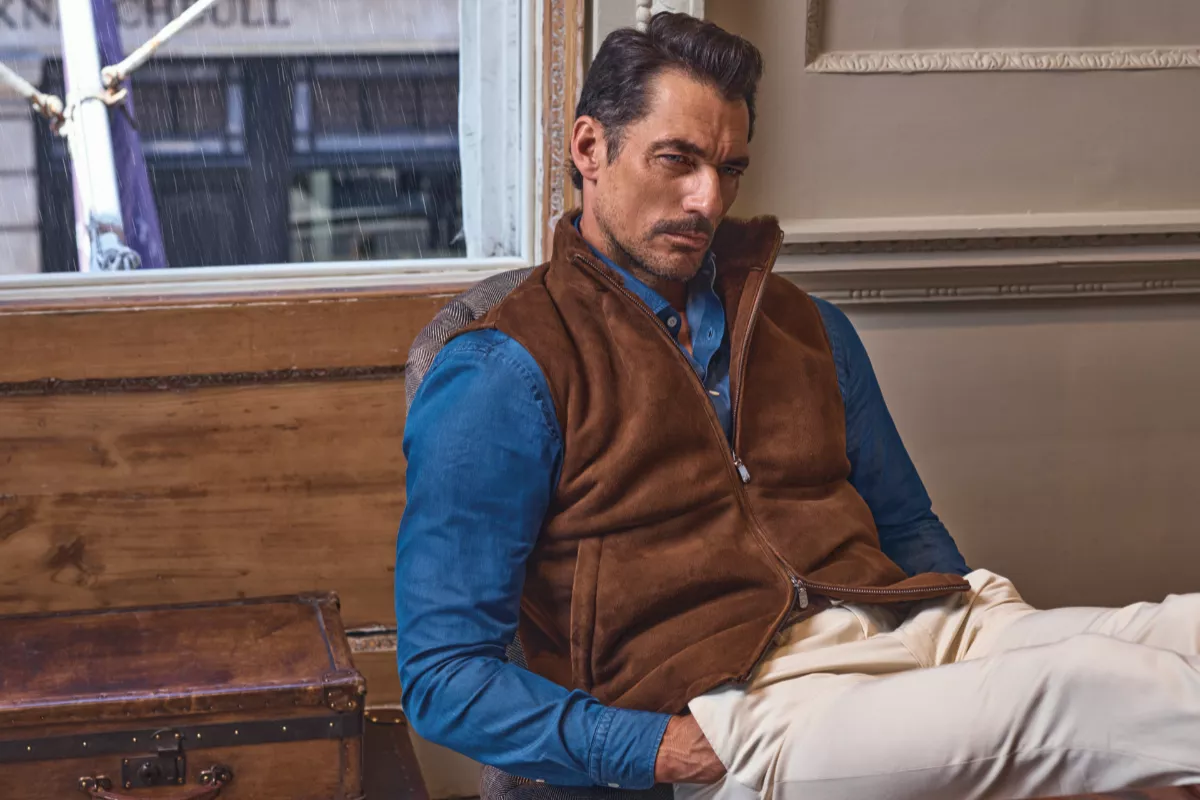 Foto del modelo y director creativo David Gandy con un chaleco café, camisa de mezclilla azul intenso y pantalones claros de la marca Hackett.