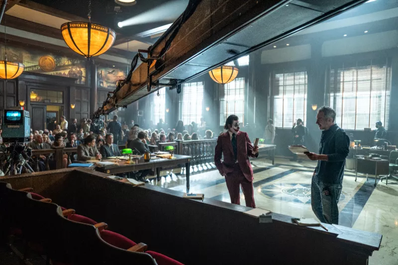 Foto de la grabación de Joker 2, con una cámara de cine arriba y Joaquin Phoenix como el Joker al centro y el director Todd Phillips a la derecha.
