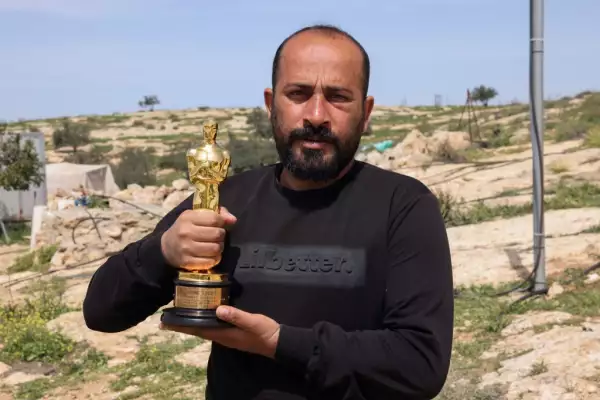 Foto de Hamdan Ballal cargando su Oscar, detrás un paisaje de Palestina.