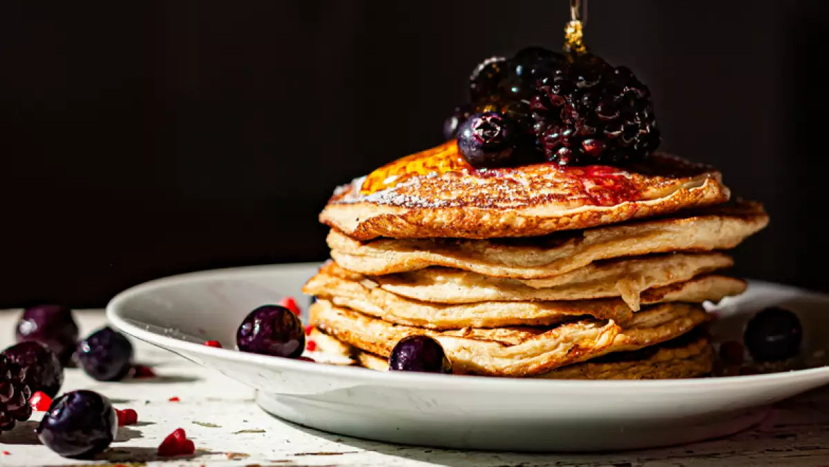 Foto de un plato con hot cakes hechos de avena, con miel y frutos rojos encima.