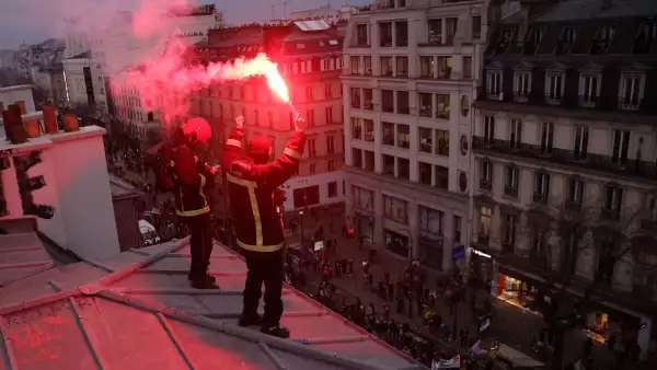 Los bomberos franceses en huelga sostienen bengalas rojas mientras se paran en la parte superior de un edificio parisino durante una manifestación como parte del noveno día de huelgas y protestas a nivel nacional contra la reforma de las pensiones del gobierno francés, en París, Francia, el 23 de marzo de 2023.