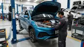 Técnico revisa un automóvil eléctrico azul dentro de un taller, con el cofre abierto y equipo de diagnóstico en mano.
