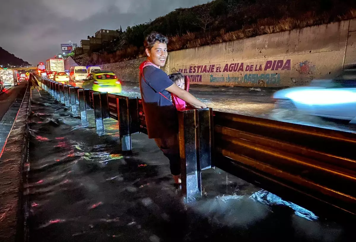 Padre cruza con su niña en pecho, una de las zonas más afectadas por las lluvias.