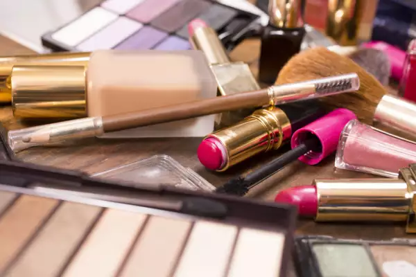 Various cosmetics, make-up lie on wooden dressing table.