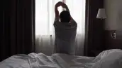 Silhouette of man sitting on bed stretching up arms