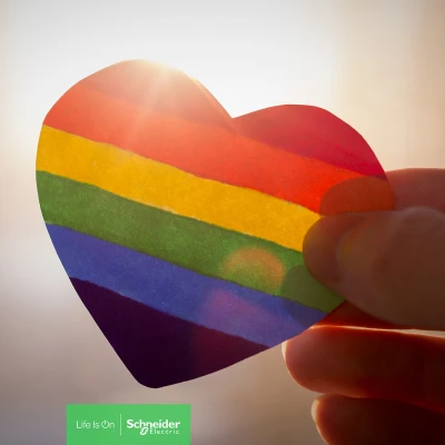 Una mano sostiene un corazón con los colores de la bandera de la comunidad LGBT+