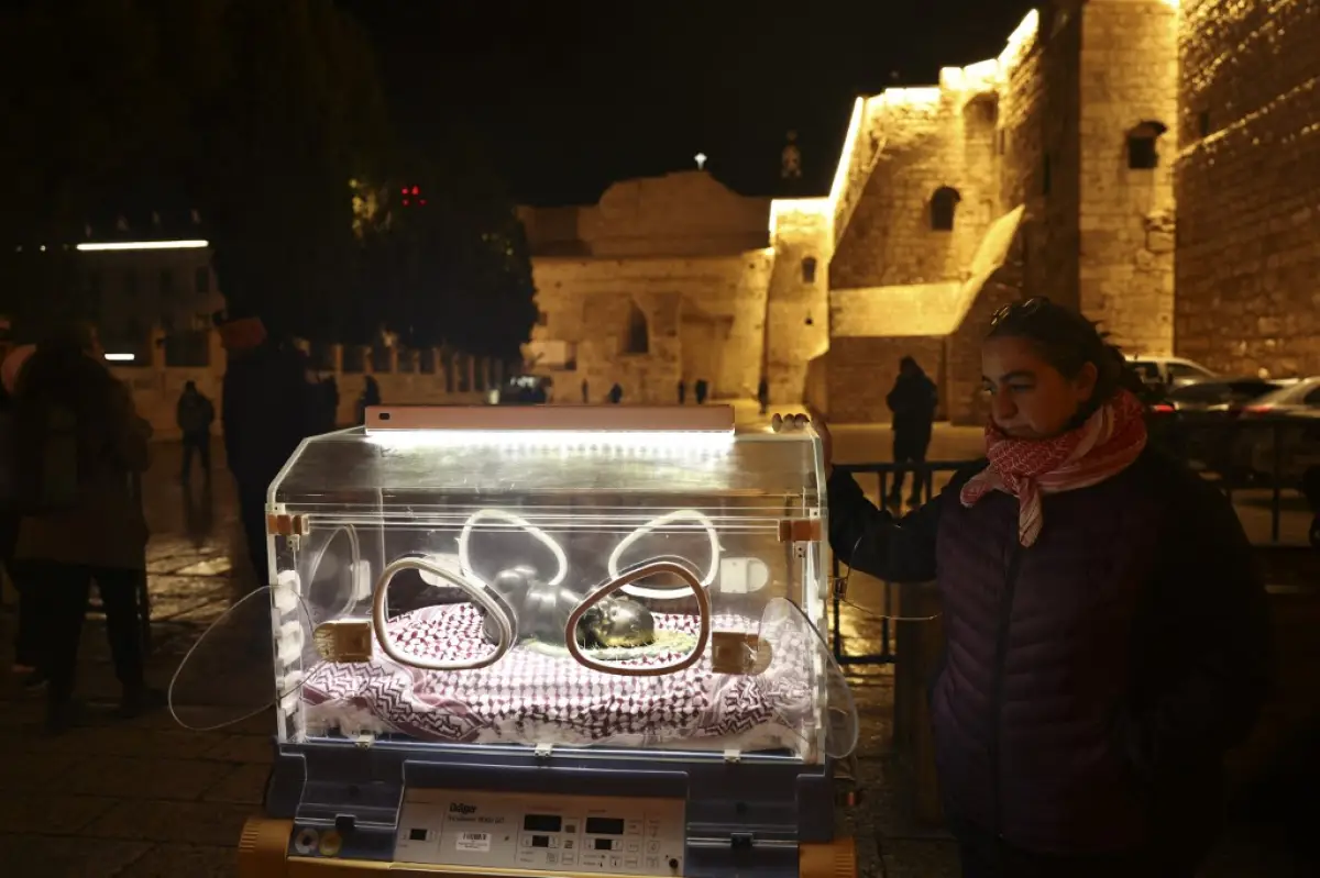 La artista palestina Rana Bishara se encuentra junto a su instalación del niño Jesús en una incubadora en la entrada de la Iglesia de la Natividad en la ciudad bíblica de Belén, en la Cisjordania ocupada, el 24 de diciembre de 2023.