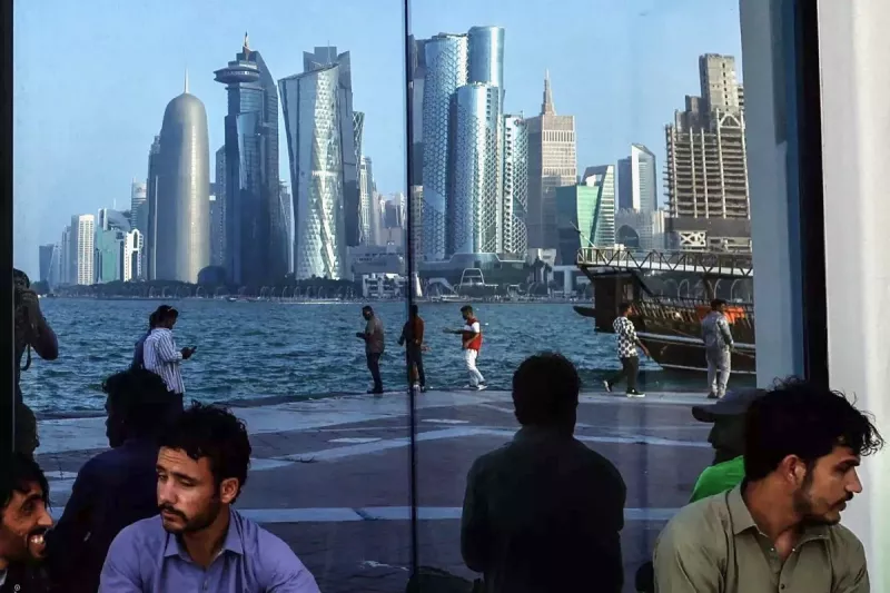 La gente se sienta con el reflejo del horizonte de Doha a lo largo de la Cornisa de Doha, en el segundo día de las celebraciones de Eid al-Fitr que marcan el final del mes sagrado musulmán del Ramadán, en Doha el 21 de marzo de 2026.