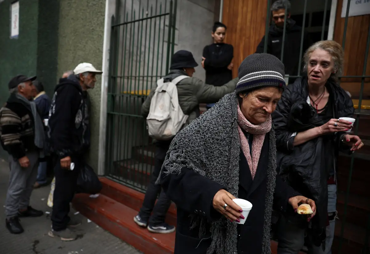 Una mujer se aleja después de recibir un refrigerio por la tarde de una iglesia que ayuda a los pobres, mientras otras personas se alinean, en Buenos Aires, Argentina, el 31 de mayo de 2024