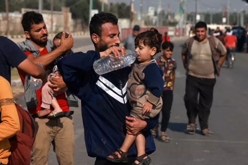 Los hombres ayudan a los niños pequeños a beber un poco de agua al llegar al centro de la Franja de Gaza a pie a través de la carretera Salah al-Din en su camino a la parte sur del enclave palestino el 5 de noviembre de 2023.