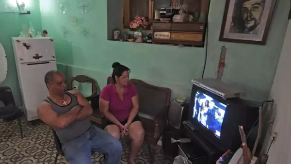 Una pareja de cubanos, acompañados por el retraro del Che Guevara, ven la transmisión de la televisión estatal