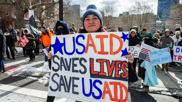 Una mujer sostiene un cartel que apoya a USAID mientras los manifestantes se manifiestan contra el presidente estadounidense Donald Trump y sus políticas durante una protesta cerca de la Casa Estatal de Massachusetts en el Día del Presidente el 17 de febrero de 2025, en Boston, Massachusetts.