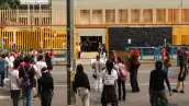 Grupo de jóvenes de espaldas frente a unas rejas amarillas de un plantel de la UNAM.jpg