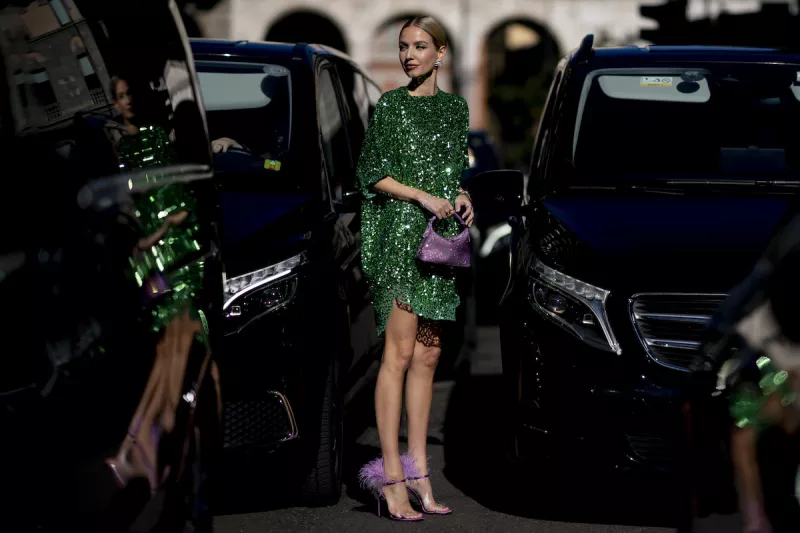 Mujer con vestido verde y sandalias con plumas en color lila. 