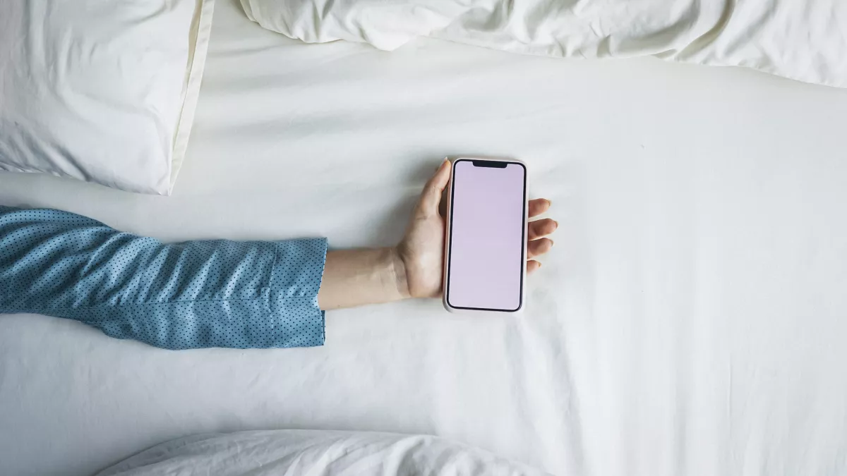 Sleeping Apps: Hand of a Woman in Pyjamas Holding a Smartphone on the Bed