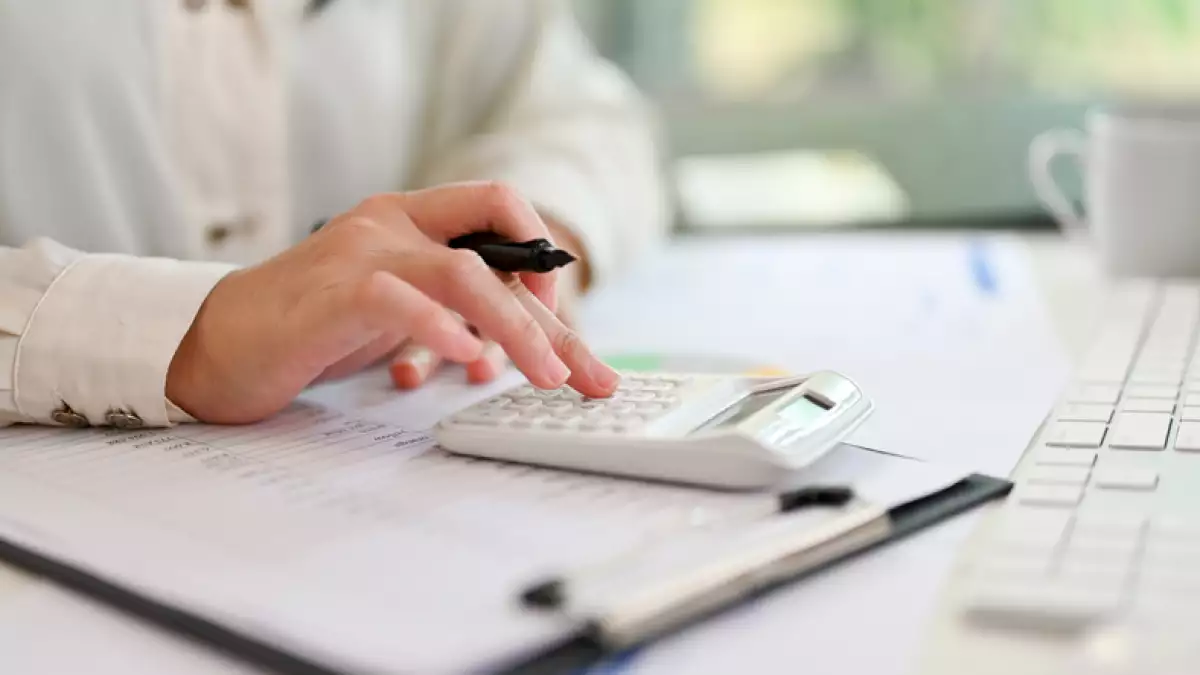 Imagen de primer plano de una mujer de negocios que usa una calculadora, trabajando en un informe financiero en su escritorio.