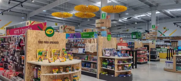 Pasillos de OfficeMax con productos de arte, diseño y material escolar, exhibidos en módulos de madera y estanterías. Se observan artículos de marcas como Crayola y Pixar, además de señalizaciones para orientar a los clientes. El espacio combina materiales creativos con otras categorías de la tienda.