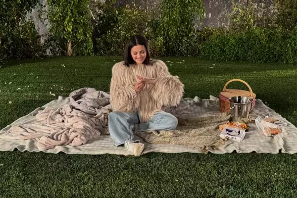 foto de selena gomez sentada entre cobijas extendidas en un jardín con una canasta de picnic a un lado.
