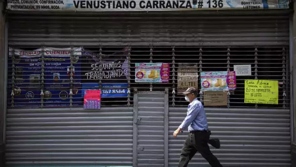 Un hombre camina por la Calle Venustiano Carranaza en el Centro Histórico, frente a el, una plaza cerrada con diversos letreros con invitaciones de los comerciantes a contactarlos vía telefónica
