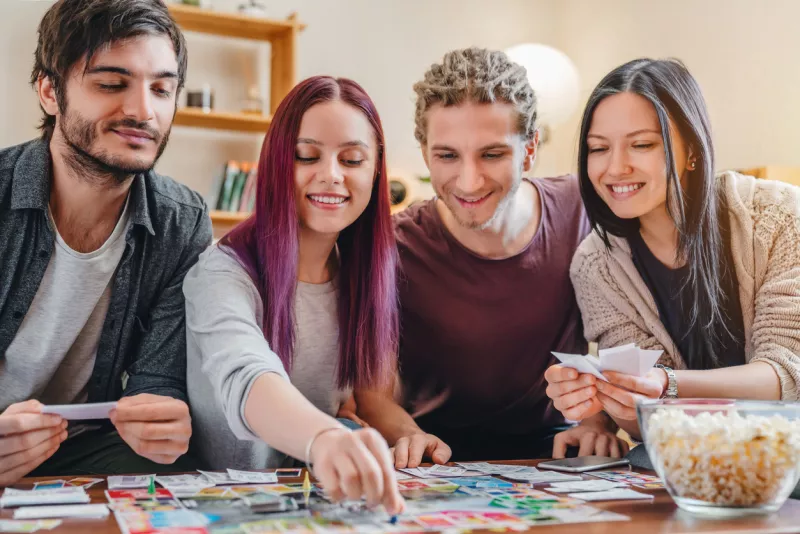 Young group of friends playing board game on table at home interior