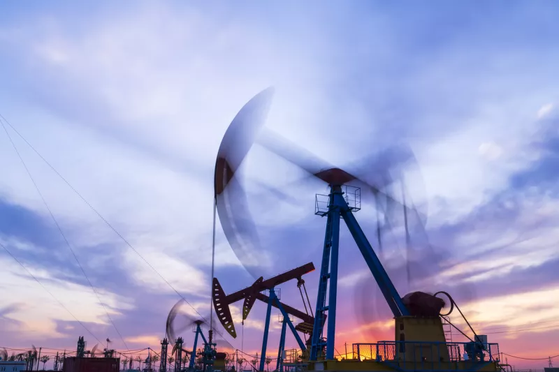Sitio del campo petrolero, por la noche, las bombas de aceite están funcionando, la bomba de aceite y la hermosa puesta de sol reflejadas en el agua, la silueta de la unidad de bombeo de vigas por la noche.