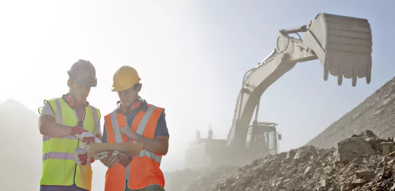 dos trabajadores de la construcción parados en una obra con escombros y maquinaria