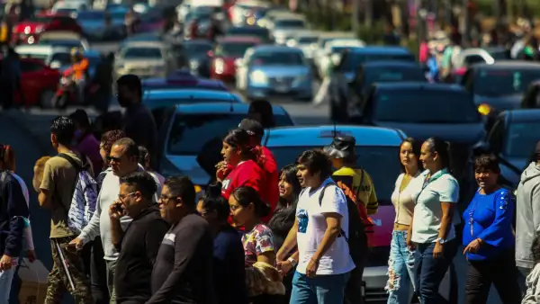 Personas cruzan una avenida frente a autos que esperan en la Ciudad de México.