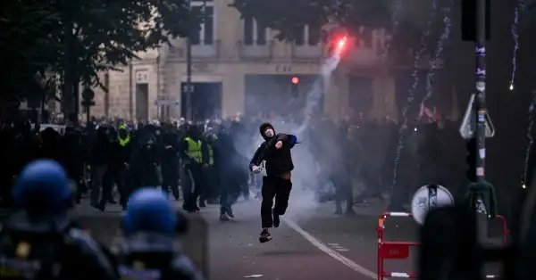 Un hombre vestido de negro lanza una bengala roja al aire. Atrás y delante aparecen policías.jpg