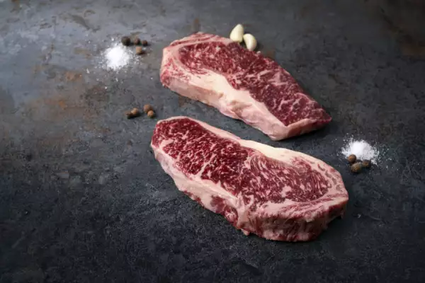 Carne Wagyu sobre tabla oscura con sal y pimientos a un lado.