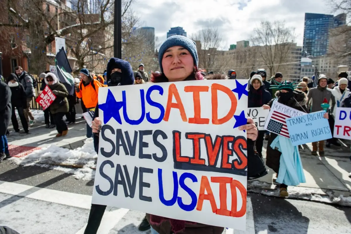 Una mujer sostiene un cartel que apoya a USAID mientras los manifestantes se manifiestan contra el presidente estadounidense Donald Trump y sus políticas durante una protesta cerca de la Casa Estatal de Massachusetts en el Día del Presidente el 17 de febrero de 2025, en Boston, Massachusetts.