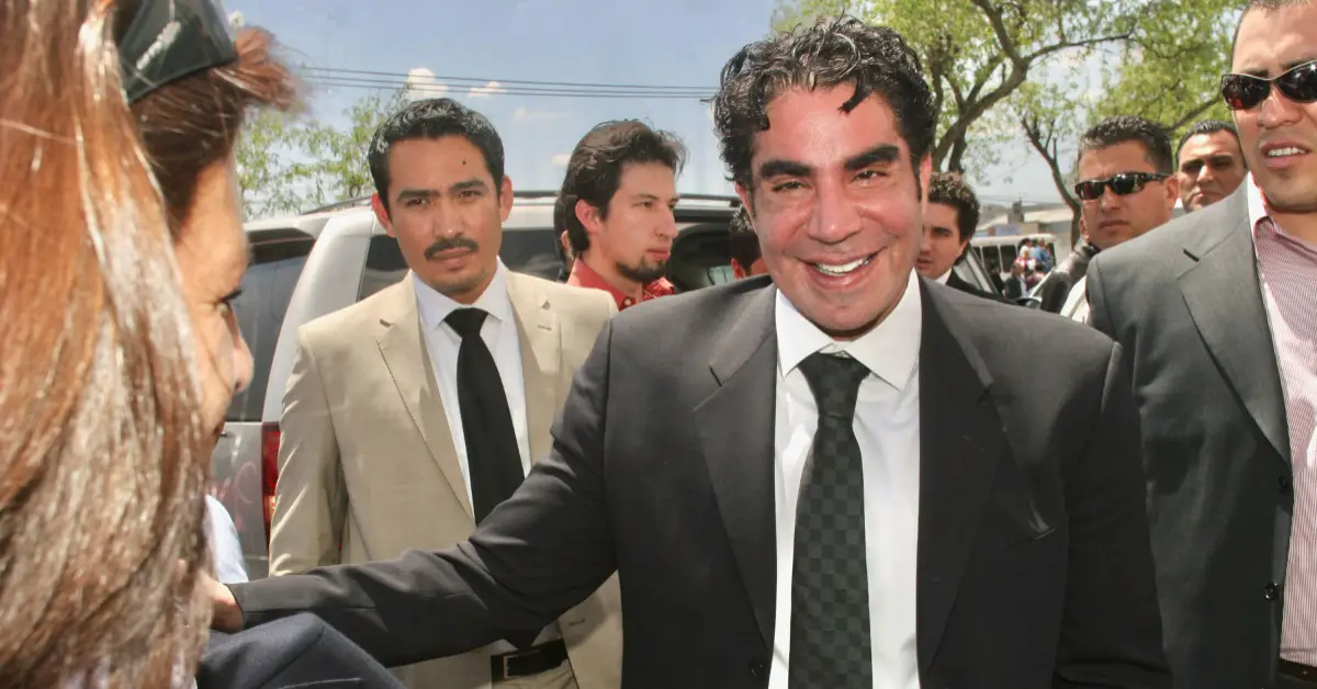 Jorge Kahwagi vestido de traje negro y con una sonrisa. Detrás de él otros hombres con traje.jpg