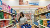Pasillo de productos como arroz, frijoles y galletas de una Superfarmacia de Farmacias Guadalajara, en el que una mujer delgada de cabello largo toma con la mano derecha un limpiapisos de envase color azul, mientras que en su brazo izquierdo sostiene una canasta con productos entre ellos unas galletas de chismas de chocolate.