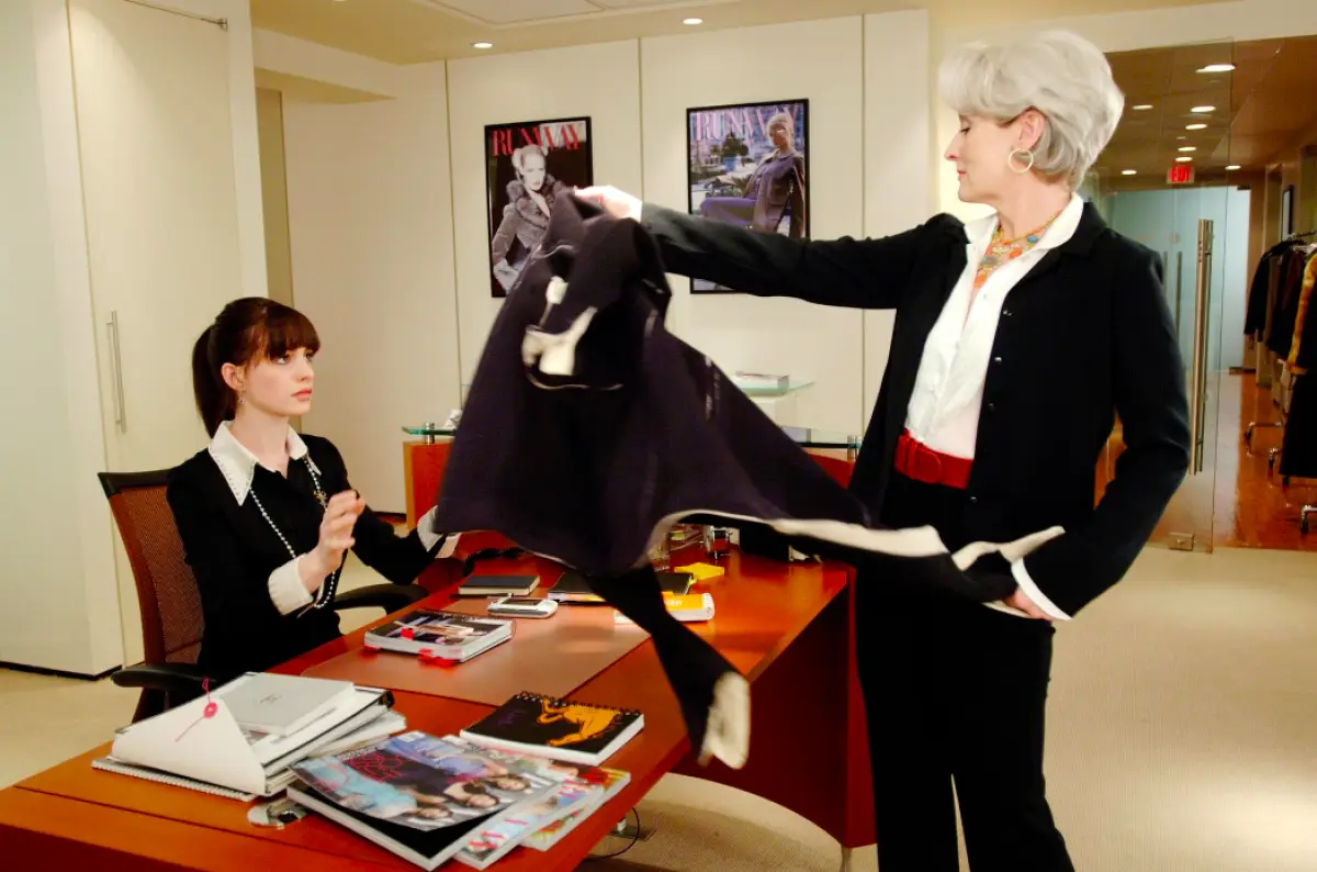Foto de Anne Hathaway y Meryl Streep en la película 'El diablo viste a la moda' cuando la editora Miranda Priestly lanza su abrigo sobre el escritorio de su asistente Andy Sachs.