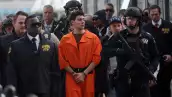 Foto de Luigi Mangione esposado, vistiendo el uniforme anaranjado de prisionero y rodeado de policías poco después de su detención.
