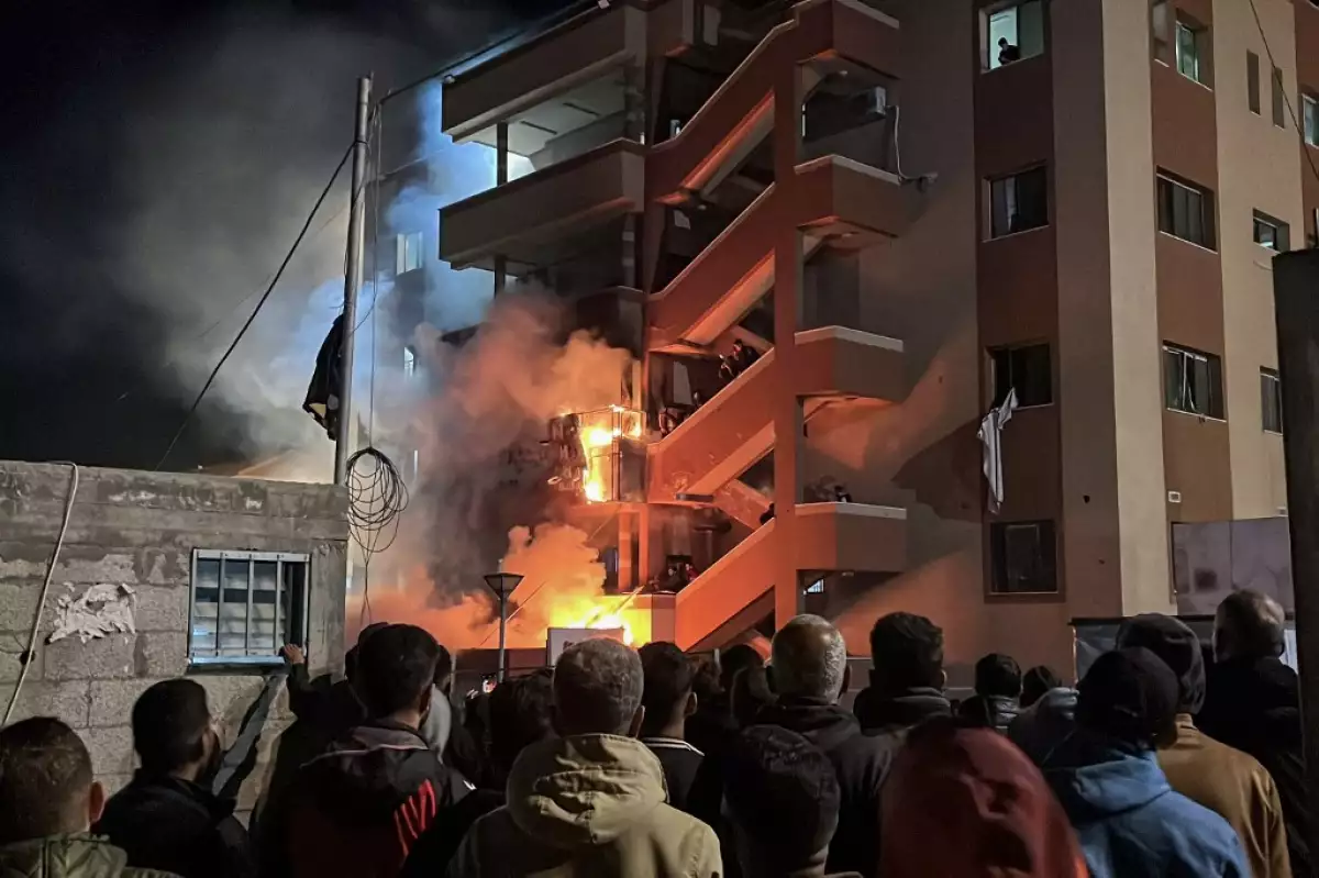 Los palestinos observan cómo la gente intenta apagar un incendio en el departamento de emergencias del hospital Nasser después de que fuera golpeado en un ataque aéreo israelí, en Khan Yunis, en el sur de la Franja de Gaza, el 23 de marzo de 2025.