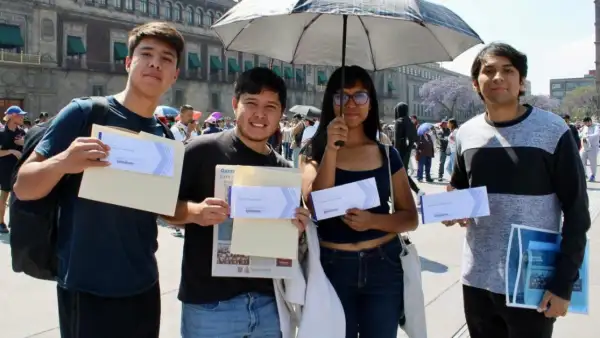 Tres hombres yuna mujer joven que muestran un sobre. Están en la plancha del Zócalo de la CDMX bajo el sol.jpg