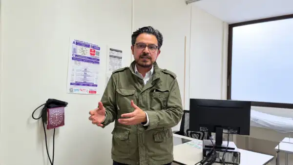 Zoé Robledo, director general del IMSS, habla frente a una cámara en un consultorio médico, con equipo de atención y una computadora al fondo.
