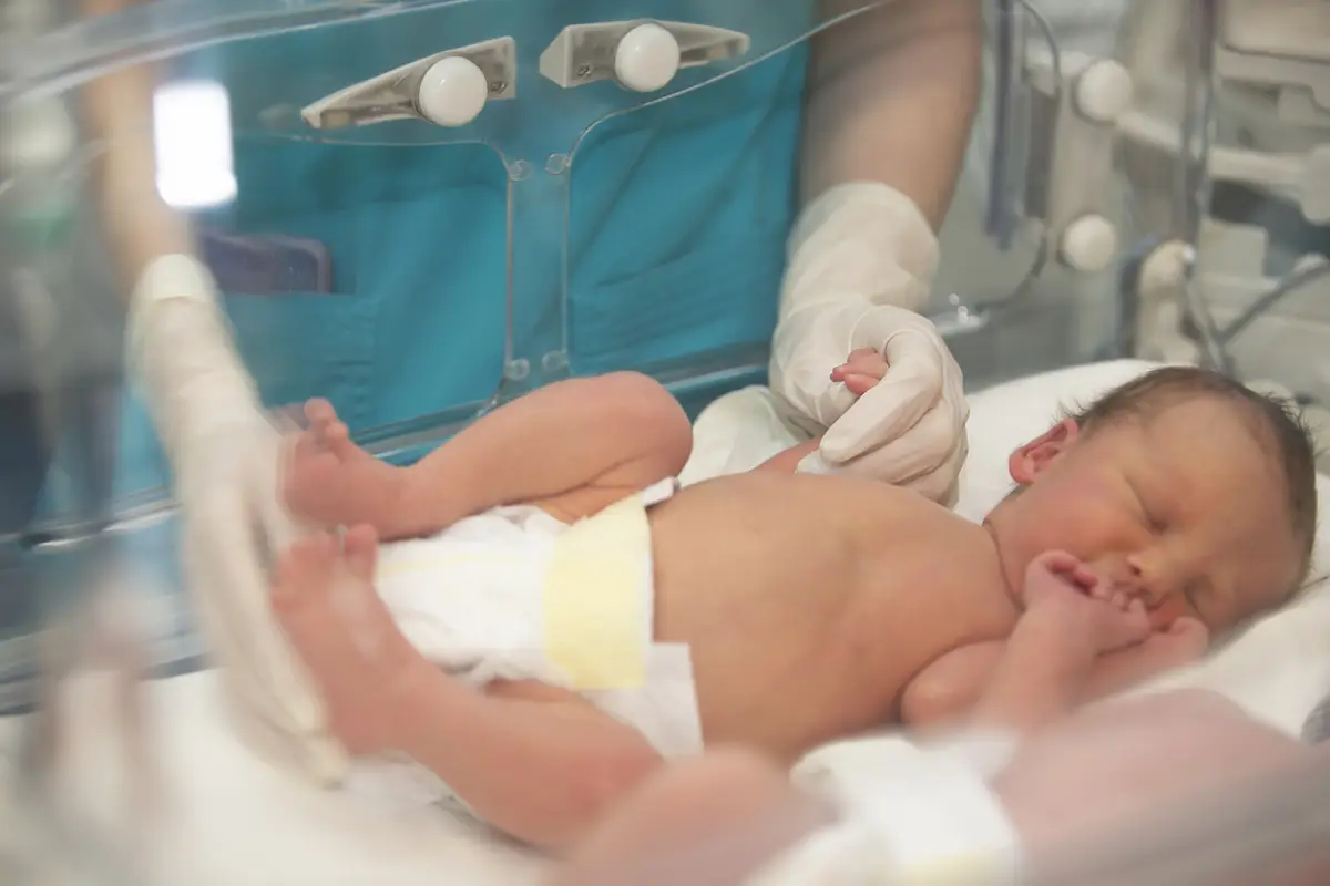 Las manos del médico con guantes de goma sostienen los dedos pequeños de un bebé recién nacido que está acostado en la caja médica.