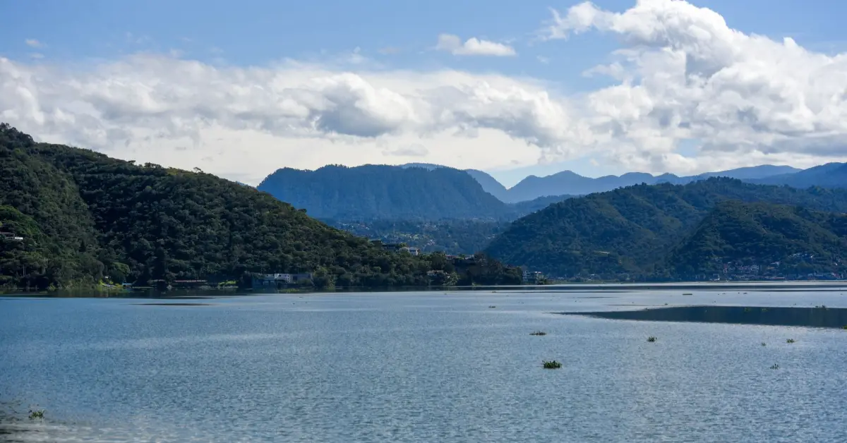Un cuerpo de agua rodeada de tres montañas de color verde bajo un cielo con nubes blancas.jpg