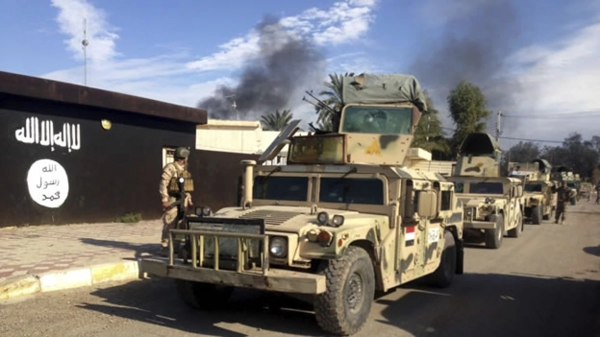 Coches militares del ejército iraquí pasan por un edificio pintado con la bandera de ISIS tras la recuperación de la ciudad de Al Saadiya, Iraq