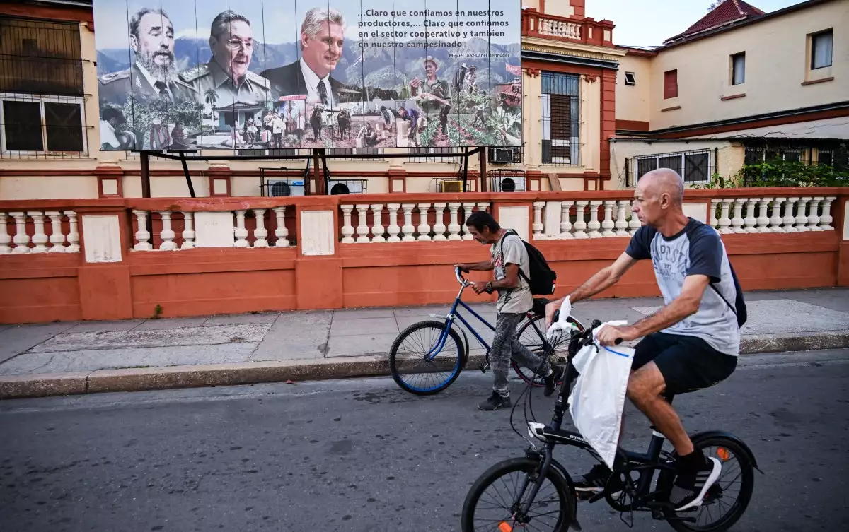 Dos hombres pasan en bicicleta por una valla publicitaria que representa al difunto líder cubano Fidel Castro, al expresidente Raúl Castro y al presidente Miguel Díaz-Canel en La Habana el 16 de febrero de 2026.