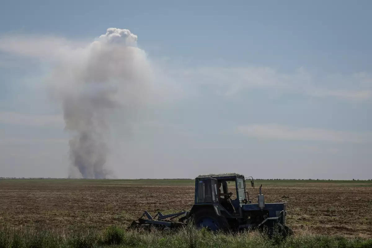 Un trabajador agrícola opera un tractor a medida que el humo aumenta en la distancia después de un ataque militar, en medio del ataque de Rusia contra Ucrania, en la región de Kherson, Ucrania, el 20 de junio de 2023.