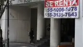 Una persona entra a un edificio del cual cuelga una gran lona con el anuncio 'se renta'.