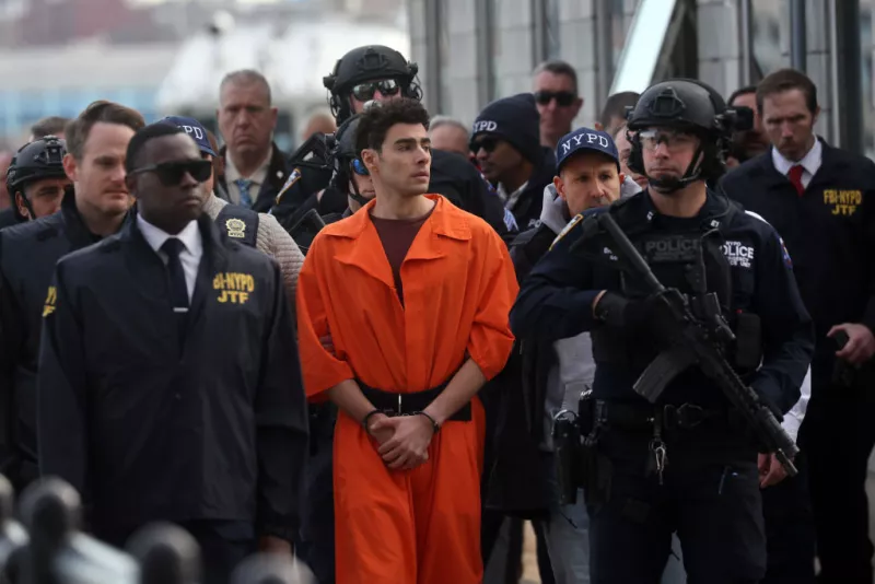 Foto de Luigi Mangione esposado, vistiendo el uniforme anaranjado de prisionero y rodeado de policías poco después de su detención.