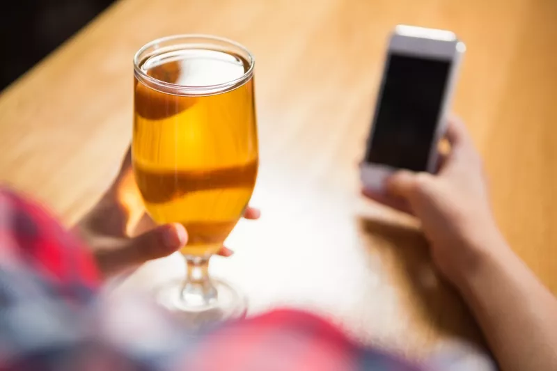 Mujer usando su celular con un vaso ddee cerveza en la mano