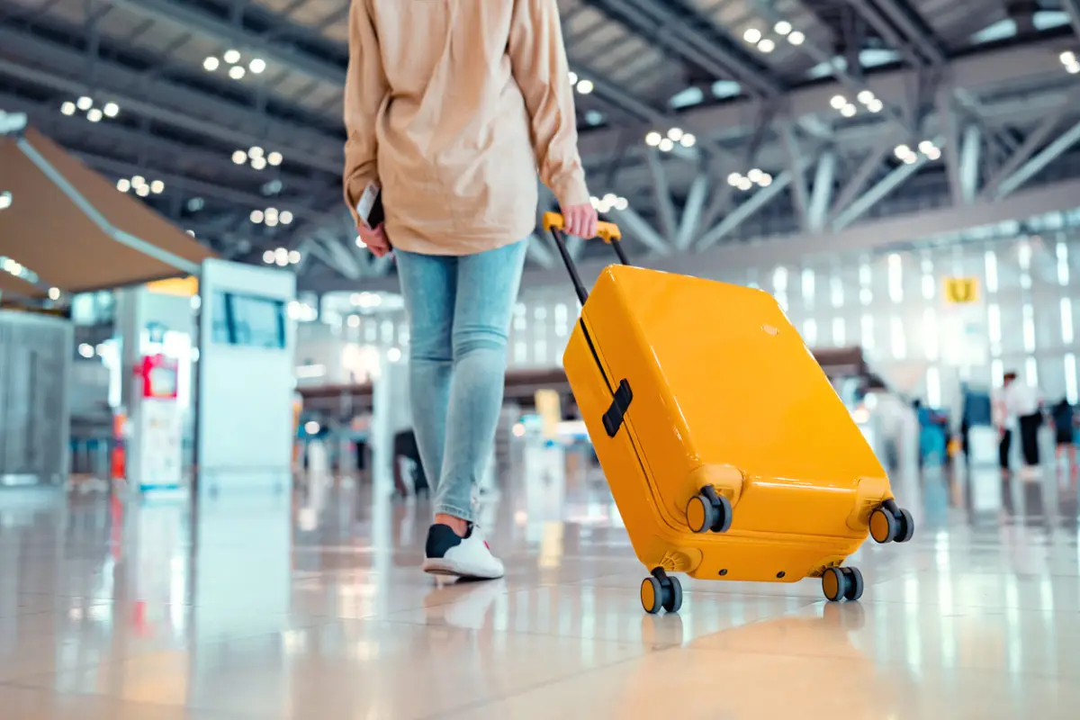 Joven pasajera viajera caminando con una maleta amarilla en la moderna terminal del aeropuerto, mujer camino a la puerta de embarque del vuelo, lista para viajar o viajar de vacaciones
