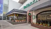 :Fachada de un restaurante Italianni’s en un centro comercial, con ventanales amplios, jardineras, detalles de ladrillo y piedra, y letreros con el nombre de la marca.