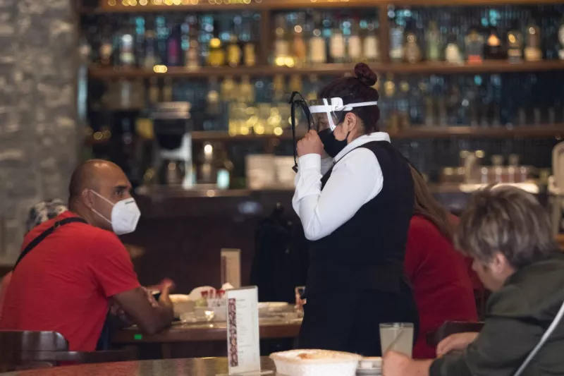 Una mesera muestra como  debe usar las caretas a unos comensales.