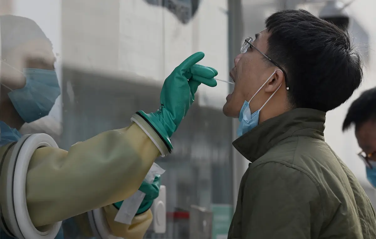 Un trabajador de la salud toma una muestra de un hisopo de un hombre para realizar la prueba del coronavirus Covid-19 en una estación de recolección de ácido nucleico en Beijing.